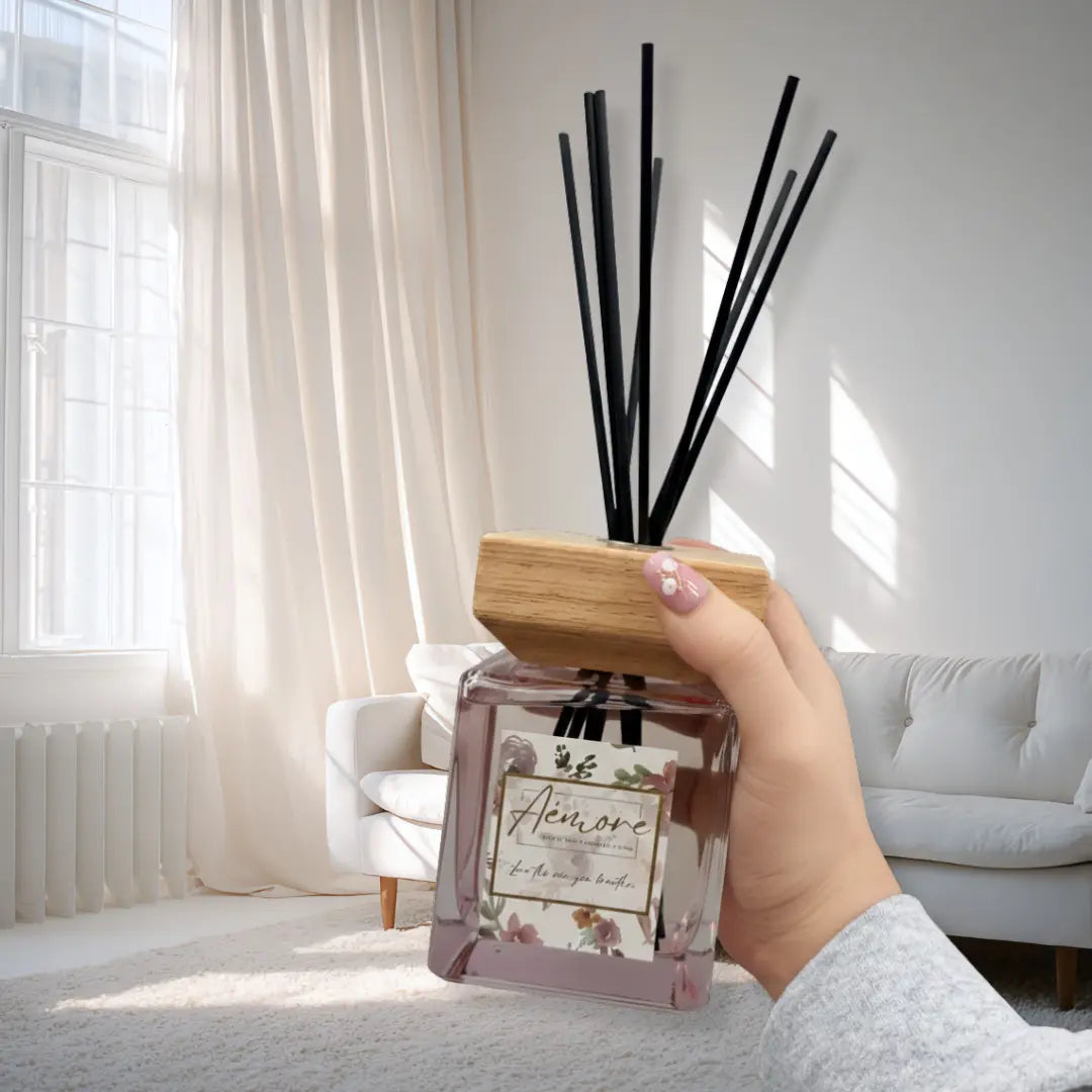 Hand holding a diffuser with black sticks in a bright living room.