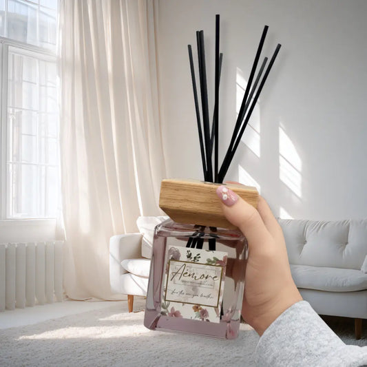 Hand holding a diffuser with black sticks in a bright living room.