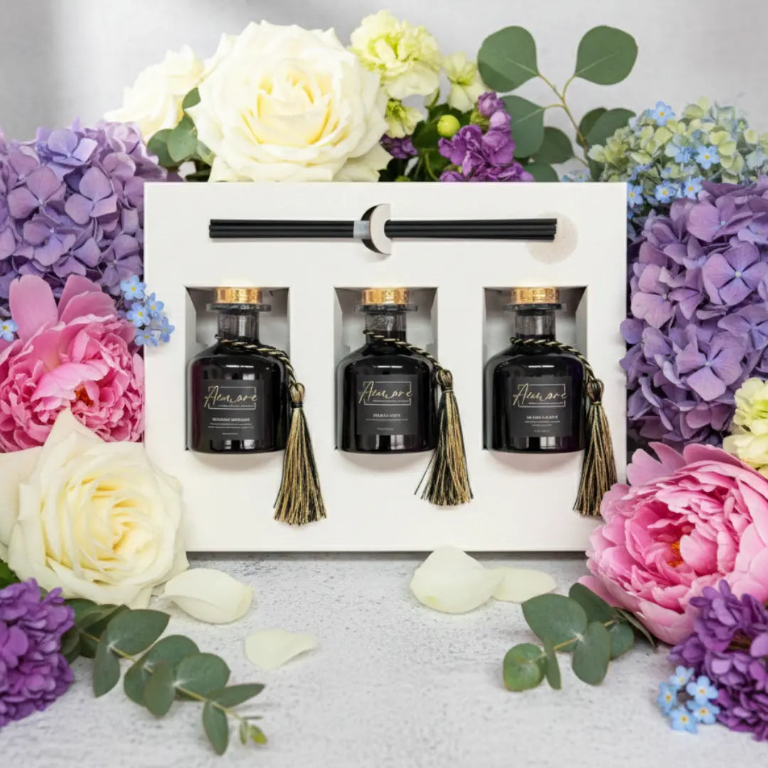 Set of three black bottles with tassels in a white box surrounded by colorful flowers.