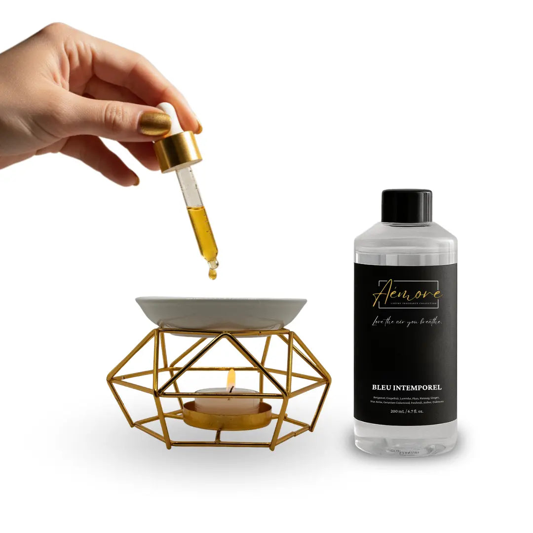 Hand using a dropper to add oil to a geometric candle holder with a bottle labeled 'Flore' on a white background.